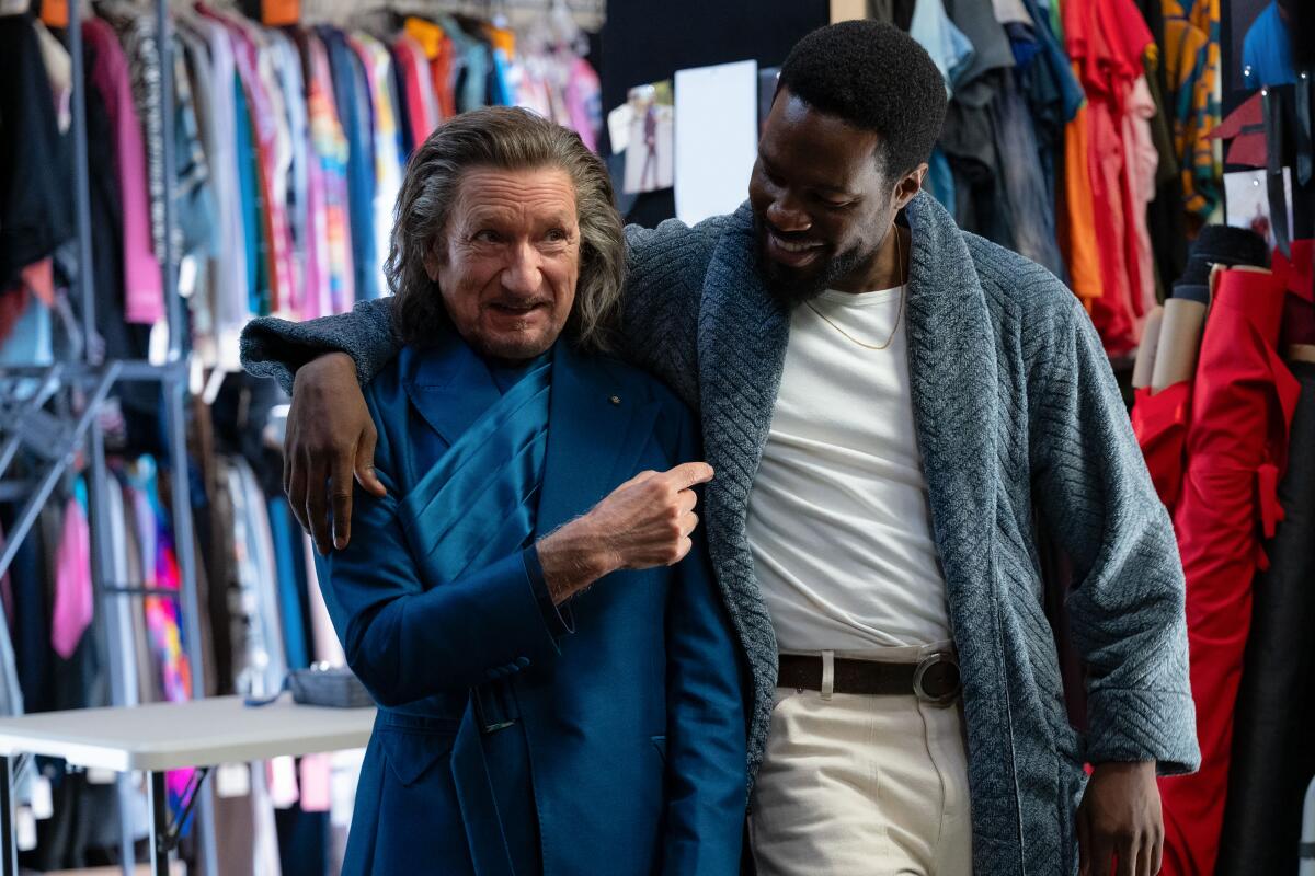 A man in a blue costume is embraced by a man in a blue robe, white T-shirt and khaki pants.