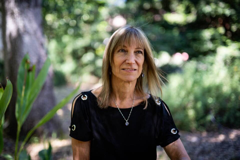 A woman wearing a black top sits in a garden