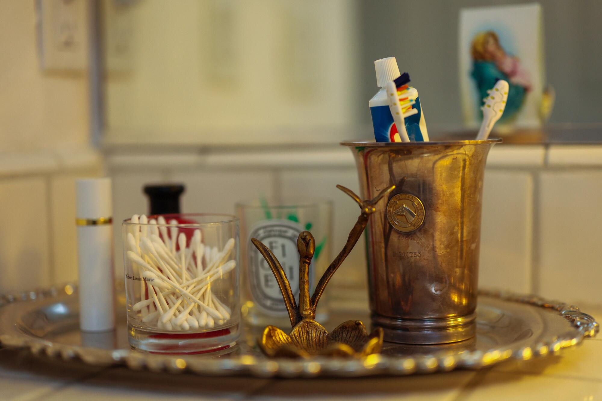 A decorative metal cup holds toothbrushes and toothpaste on top of a silver dish inside the restroom.