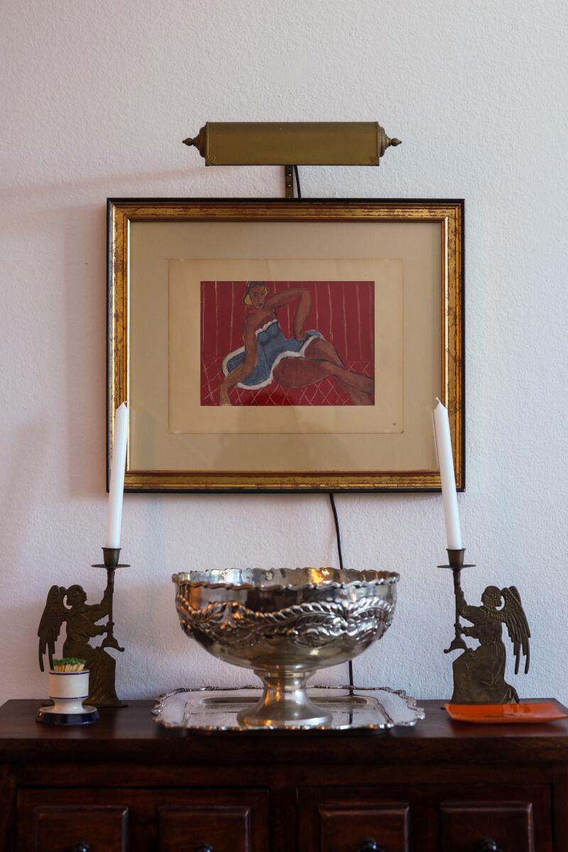 A silver punch bowl and candlesticks on a dresser underneath an artwork.