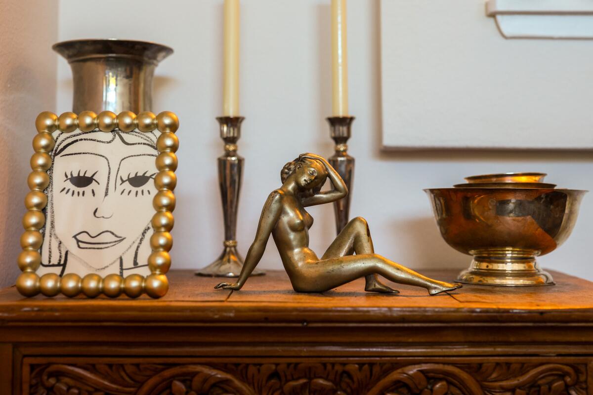 A bronze woman rest next to other second hand items on a wooden cabinet.