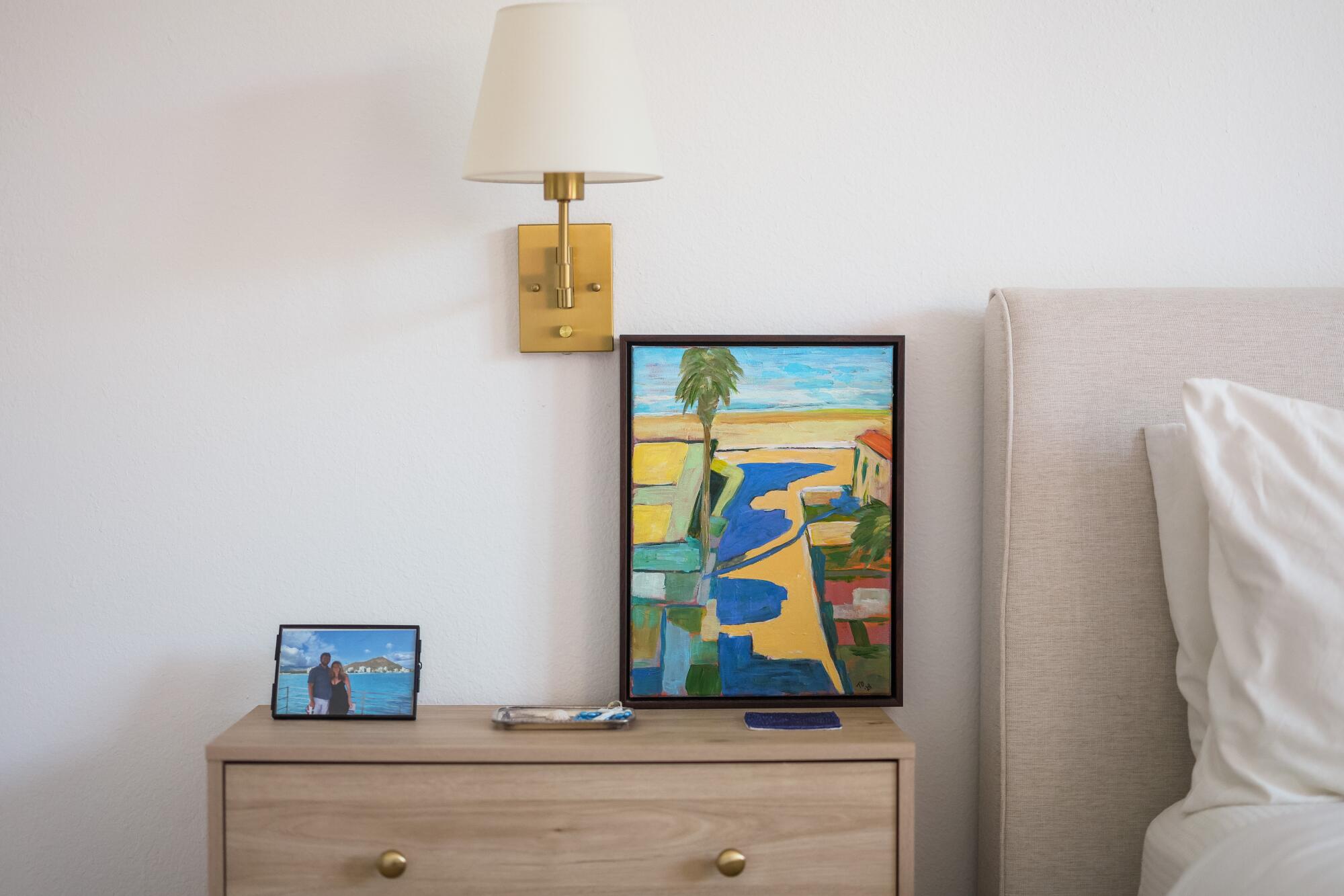  A picture of Tess van Hulsen and Andrew Chait sits next to a painting of Manhattan Beach on top of a bedside table.
