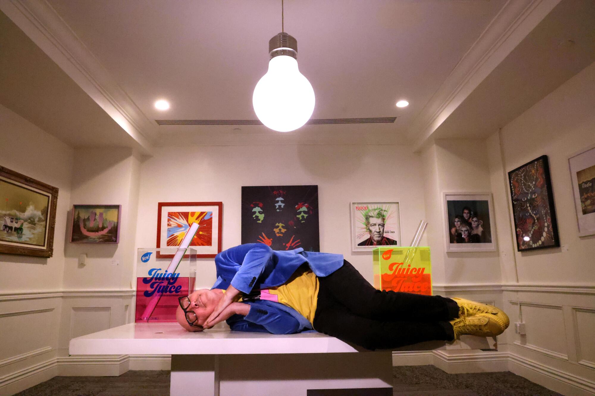 A man lays on a bench in an art gallery.