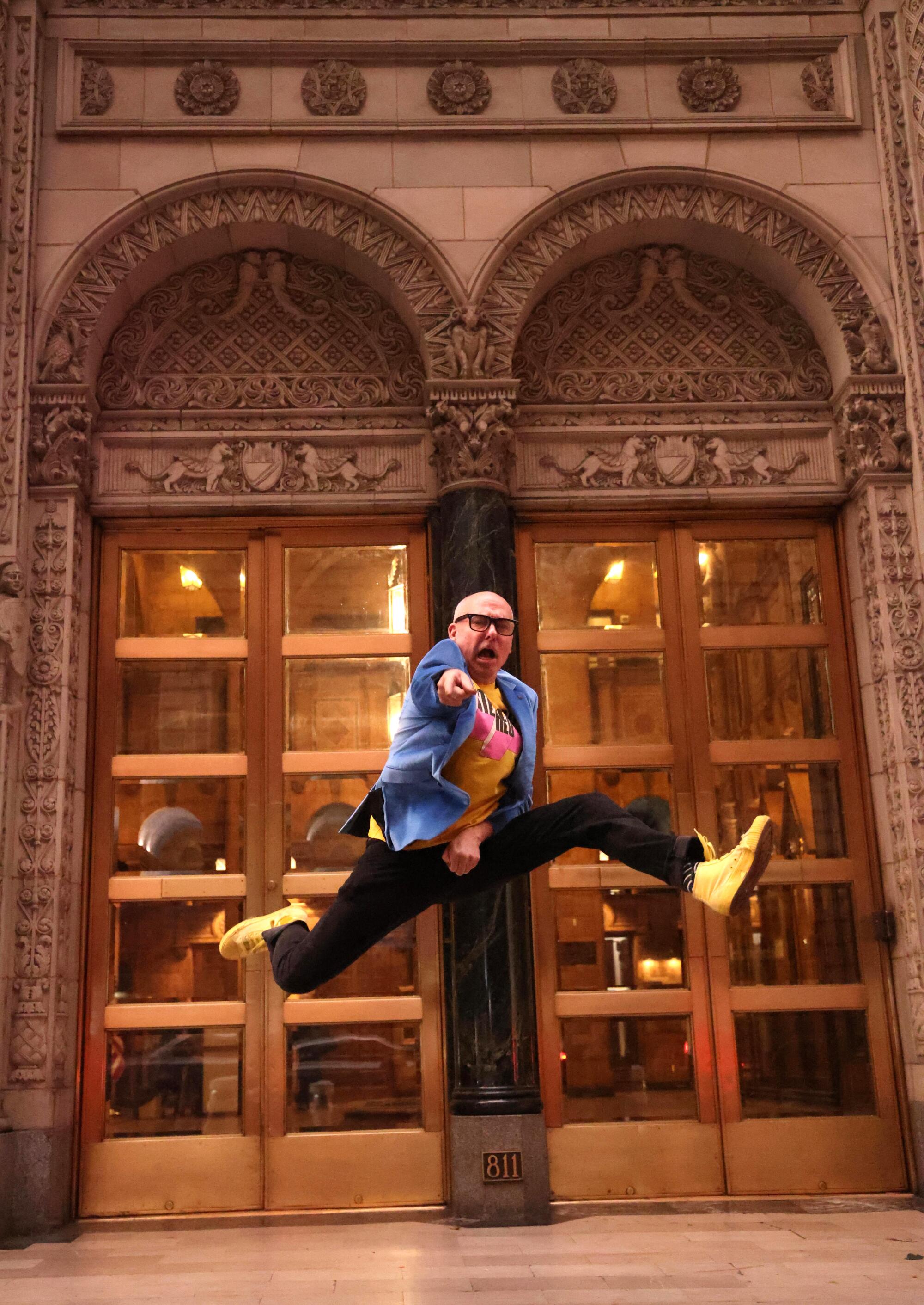 A man leaps in the air in front of a vintage building.