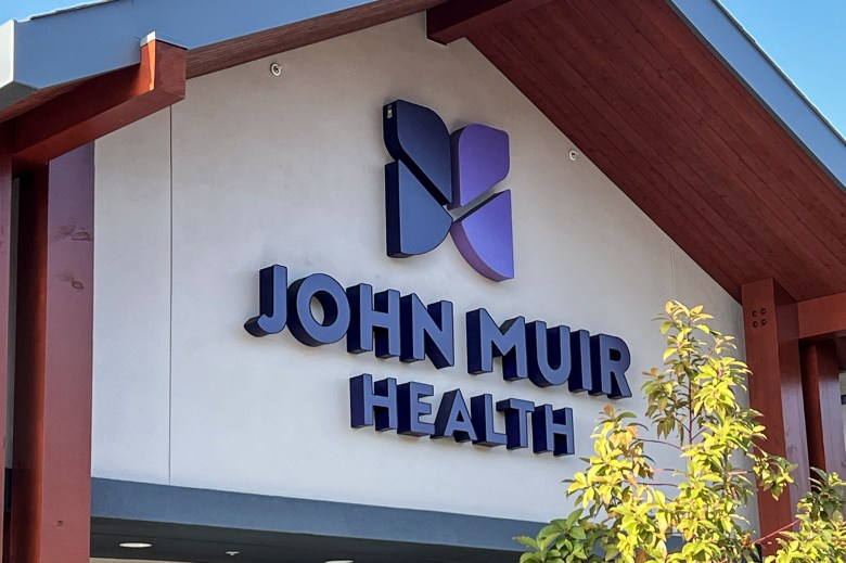 A logo for the John Muir Health facility on the façade of a beige building.