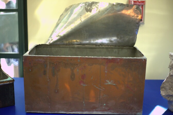 A rusted copper box has its top lifted up to see its insides. 