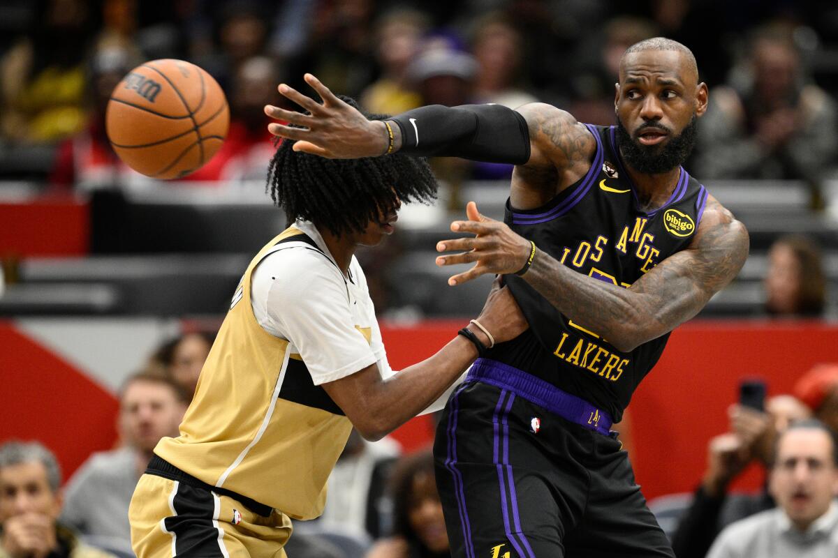 Lakers forward LeBron James, right, passes the ball behind himself and around Wizards guard Bub Carrington, left, on Friday.