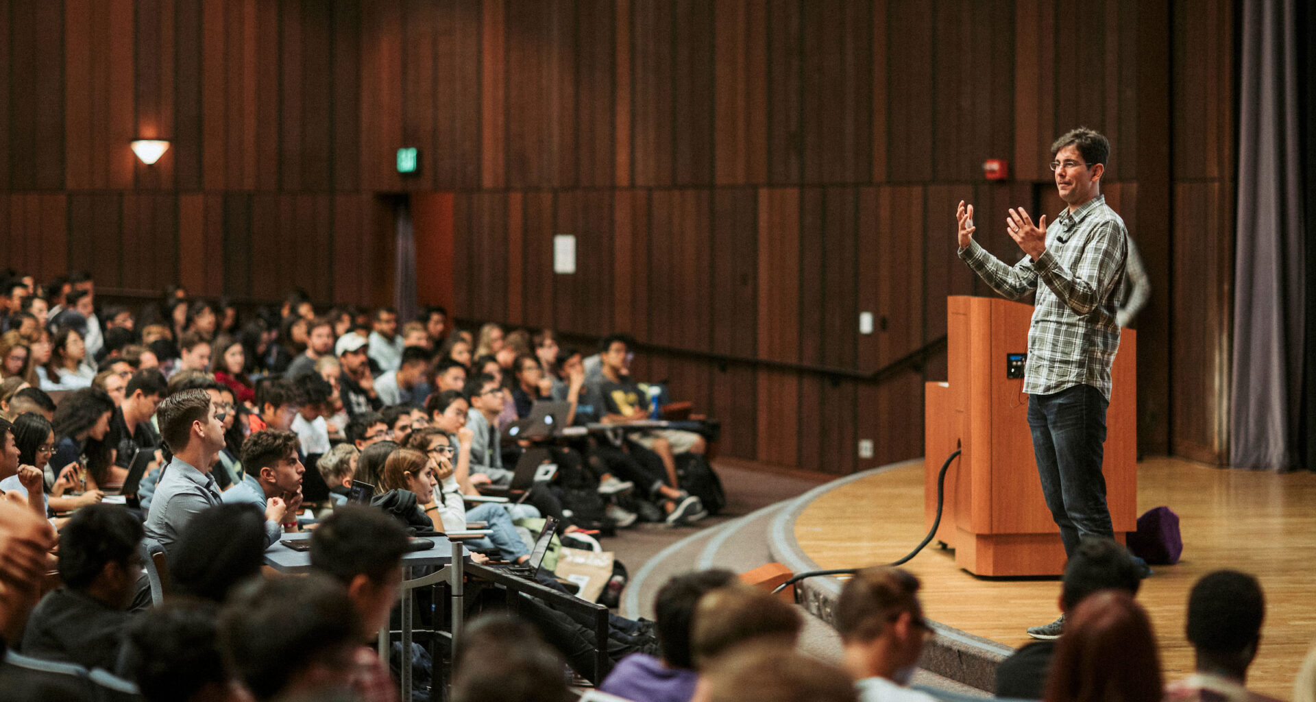 John DeNero, associate teaching professor of electrical engineering and computer sciences speaking to his class from a stage in a lecture hall.