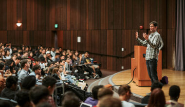 John DeNero, associate teaching professor of electrical engineering and computer sciences speaking to his class from a stage in a lecture hall.