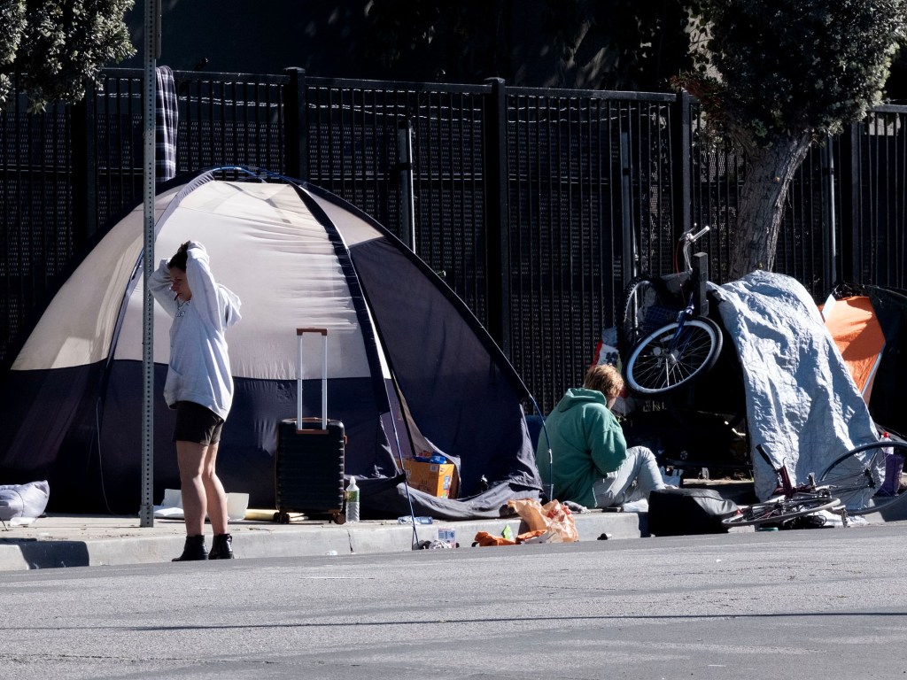 A homeless encampment in Santa Monica, with two people and tents next to a fence.