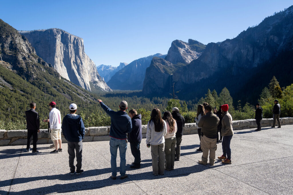 A teacher points towards Yosemite Valley in the distance as students look on