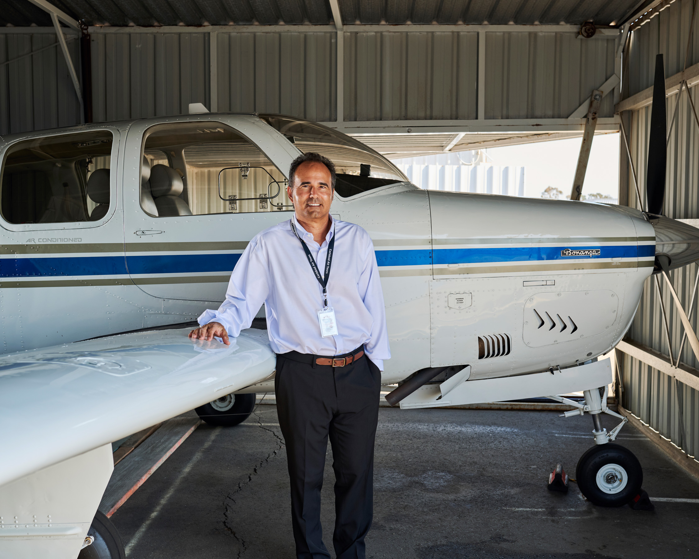 A man stands in front of a small airplane with his hand resting on the wing.