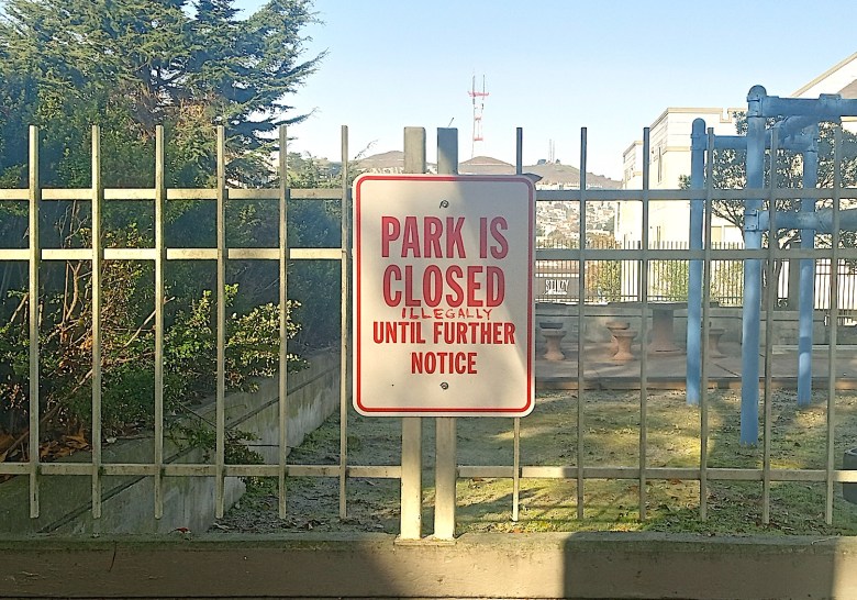 A sign on a fence that says "Park is closed until further notice." Someone has added the word "illegally" to the sign. 