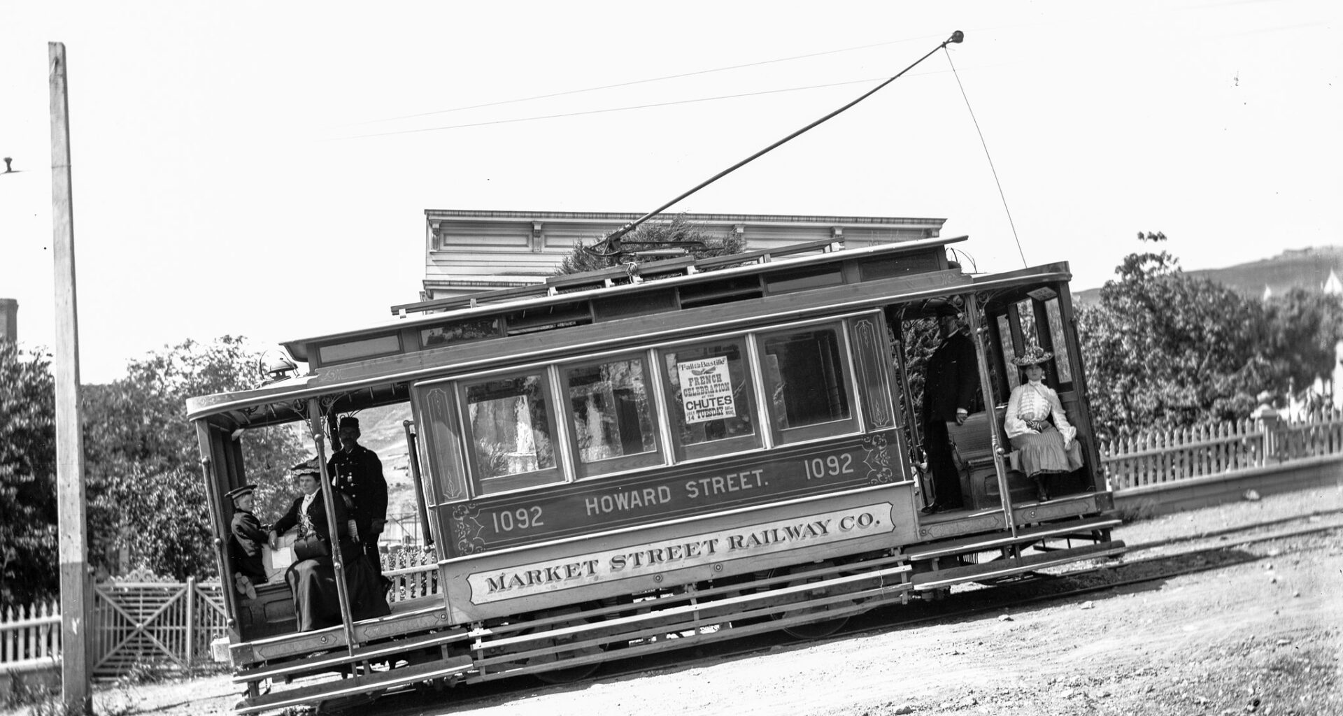 Historic streetcar labeled "Howard Street 1092" of the Market Street Railway Co. tilted on a dirt road with passengers and conductor visible.