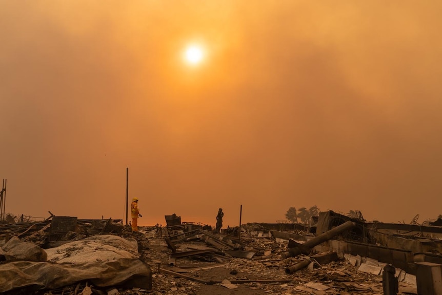  A firefighter stands among devastation with a orange sky behind. 