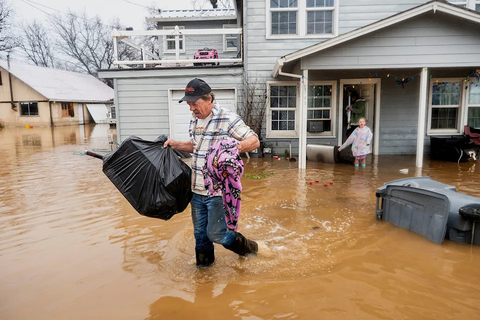 Steve Wogoman carries Christmas presents from his granddaughter's flooded home following heavy rains, on Monday, Dec. 22, 2025, in Redding, Calif. (Noah Berger / AP)