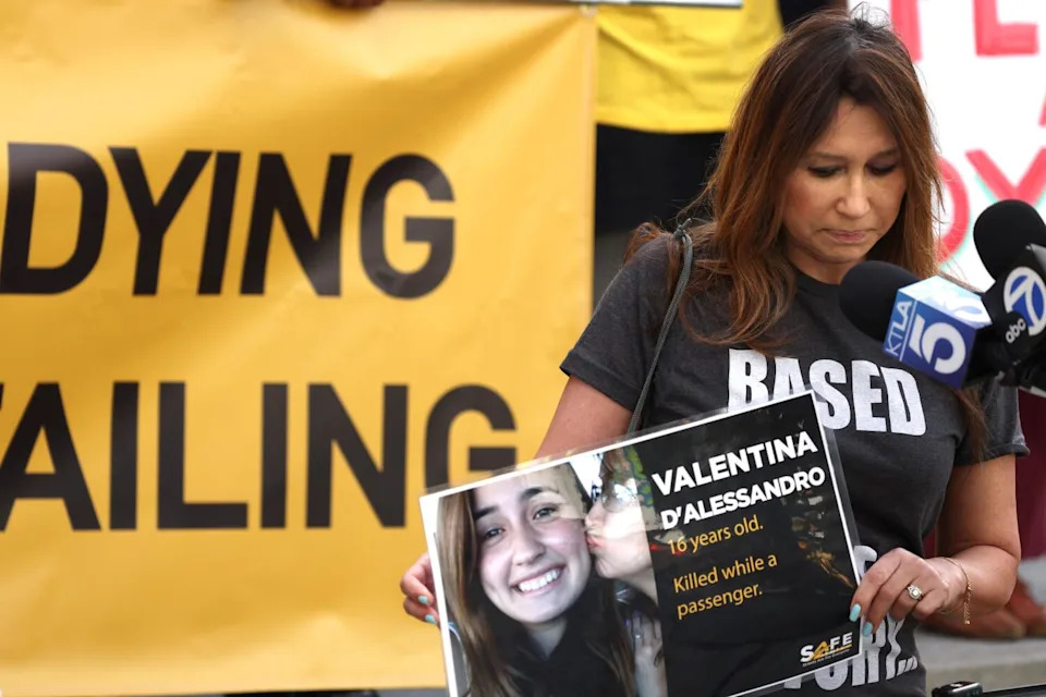 a woman looking downward while holding a poster showing a teen girl