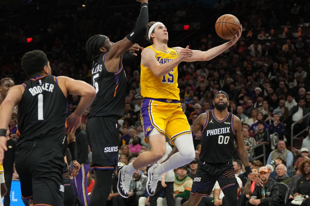 A Lakers player in a yellow jersey attempts a layup against two Phoenix Suns players in black jerseys.