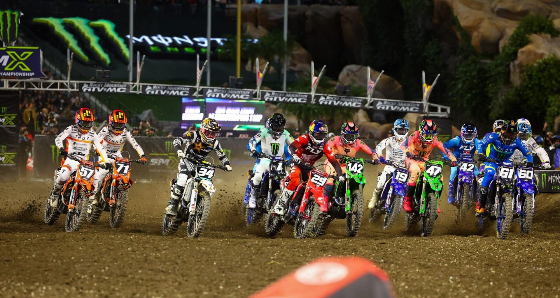 A row of dirt bikes speeds off the start grid of a supercross race.