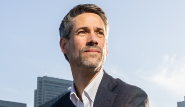 A white dome-shaped government building with columns stands before a blue semicircle, framed by a red border on the left and top sides.