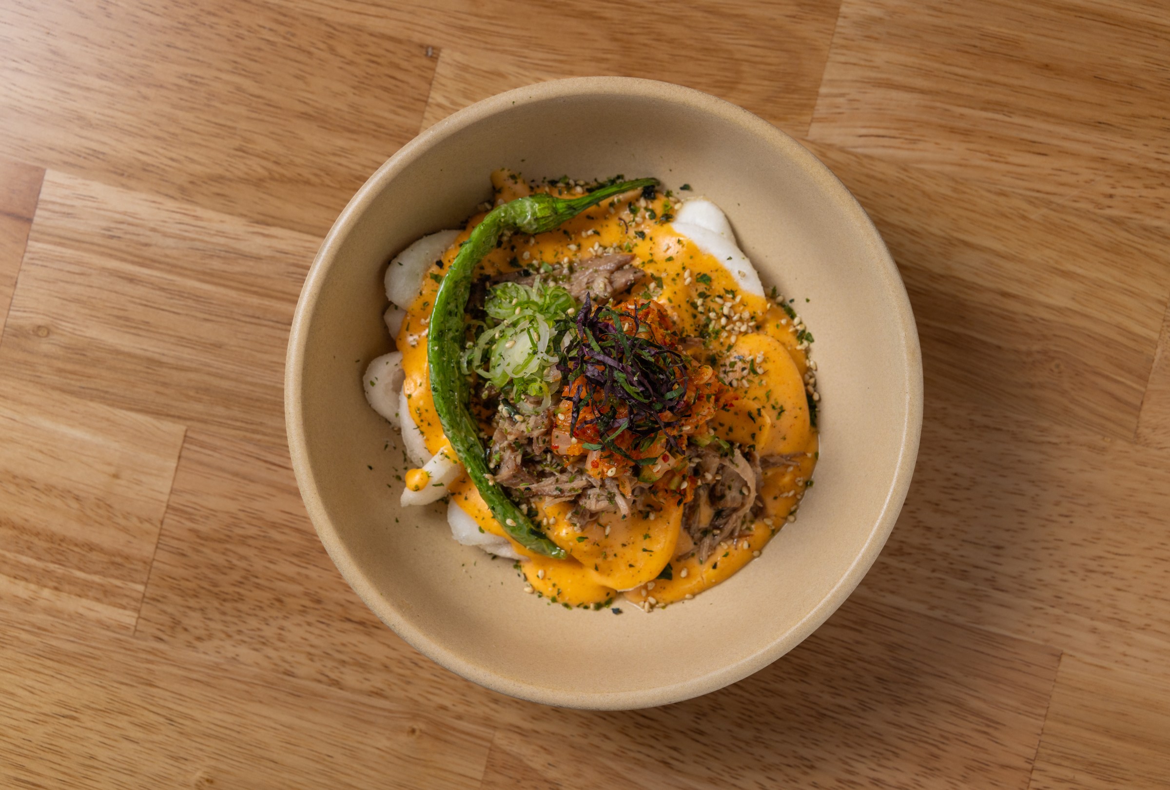 Overhead shot of Ktown nachos in a round brown bowl with rice cakes at Yi Cha