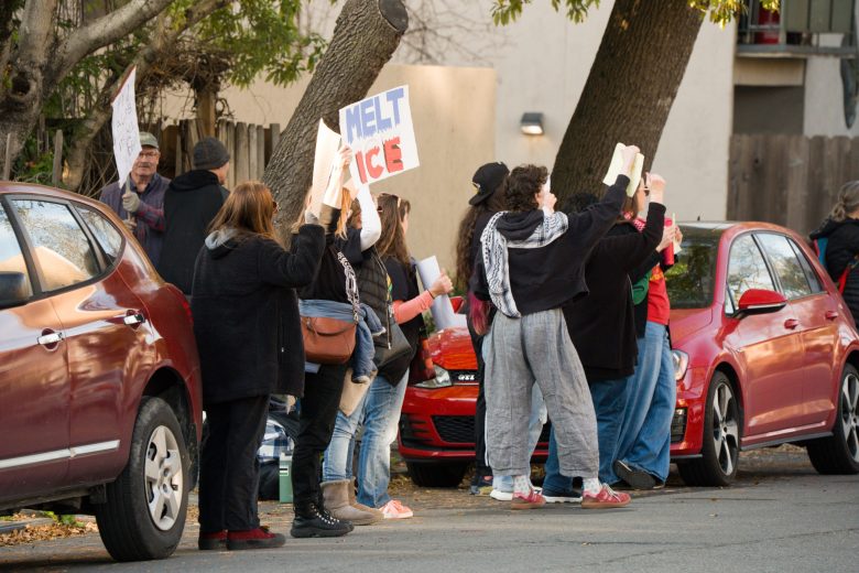 People stand in a street holding protest signs, one of which reads "melt ICE"