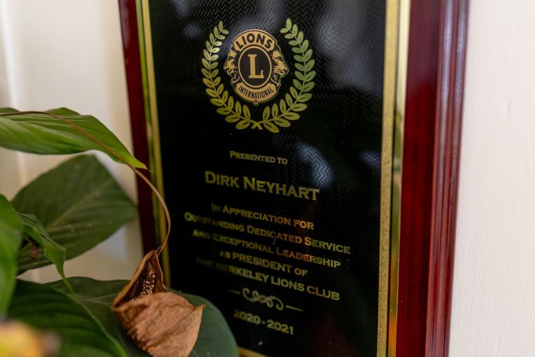 A dark wood-framed black and gold plaque honoring Dirk Neyhart for his service to the Berkeley Lion's Club.