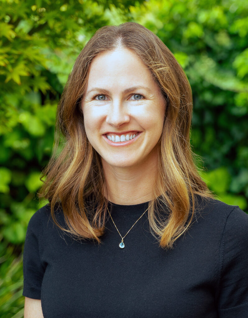 informal headshot of Dorothy Kronick, smiling, against a leafy backdrop