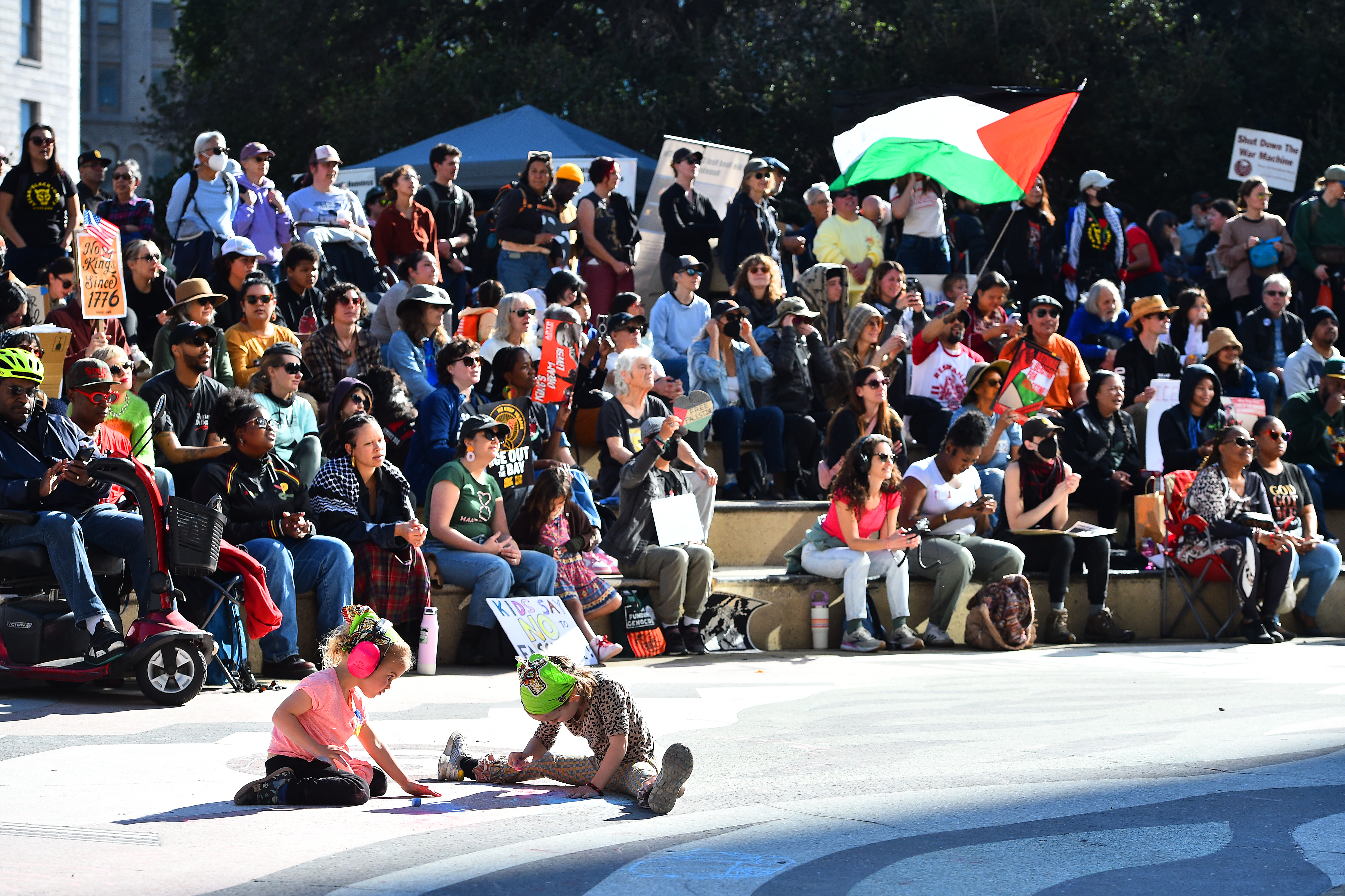 Children draw chalk drawings as people listen to speakers during...