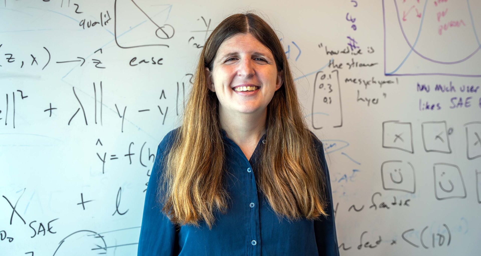 Emma Pierson stands in front of a white board that is covered in mathematical equations.