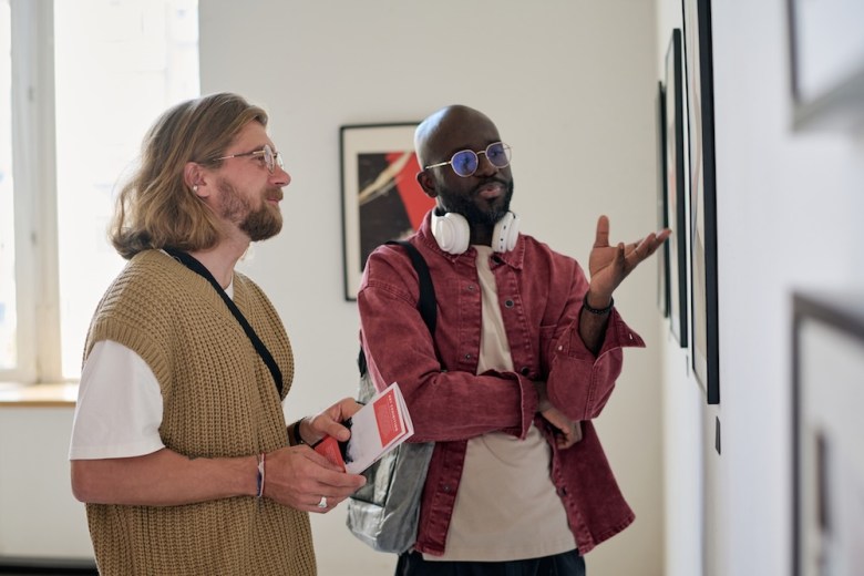 Two men discuss a piece of art in a gallery.