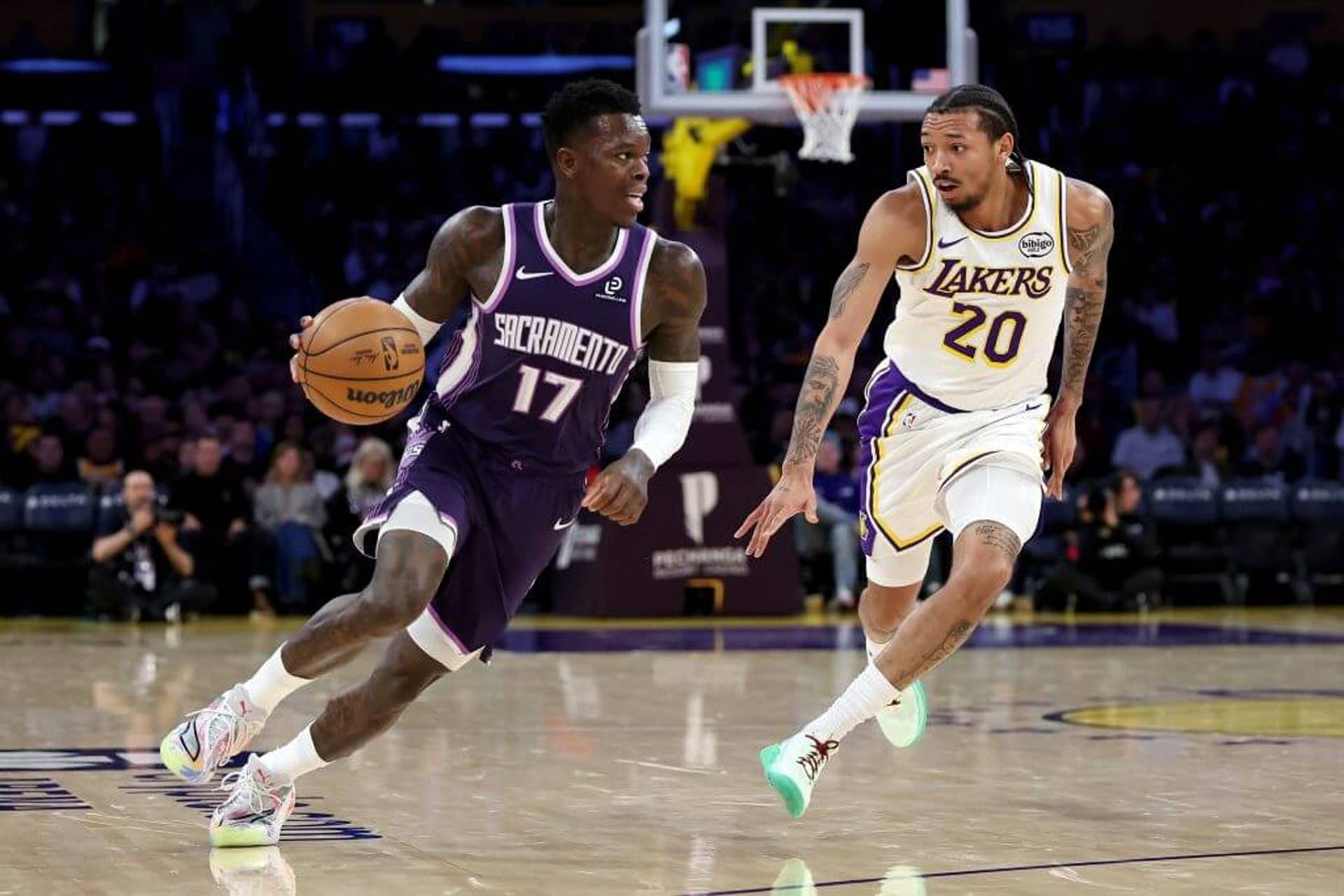 Sacramento Kings guard Dennis Schröder dribbles the ball while Nick Smith Jr. of the Los Angeles Lakers runs alongside defending.