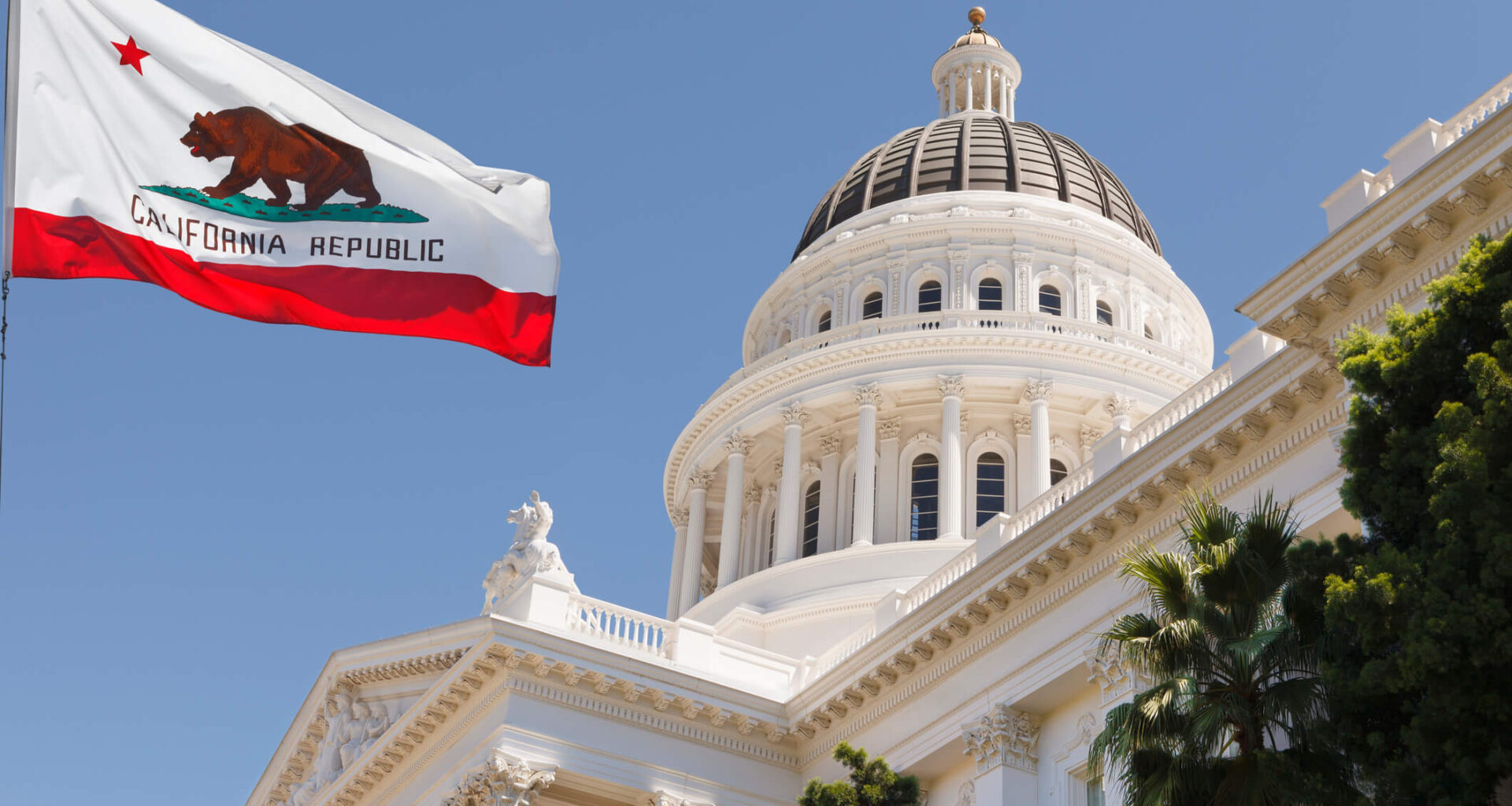 California State Capitol building with state flag in Sacramento on a windy summer day with clear sky