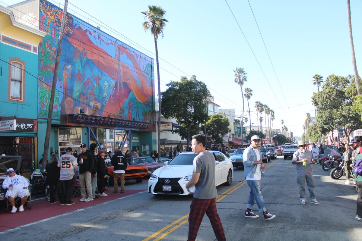 People hangout in front of the Mission Cultural Center during the lowrider tribute to Selena.