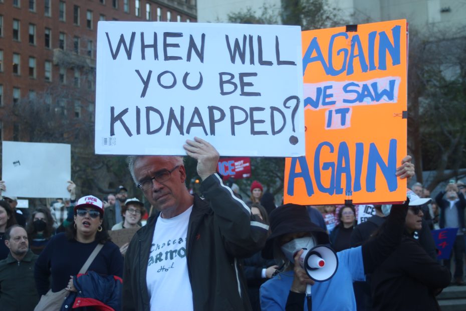A man holds a sign reading "WHEN WILL YOU BE KIDNAPPED?" beside another person with a megaphone holding a sign partially obscured that says "AGAIN WE SAW IT AGAIN" at a protest.