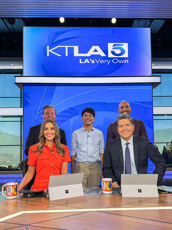 Cal State Fullerton student Raniel Santos stands amid the KTLA news team in the TV studio.