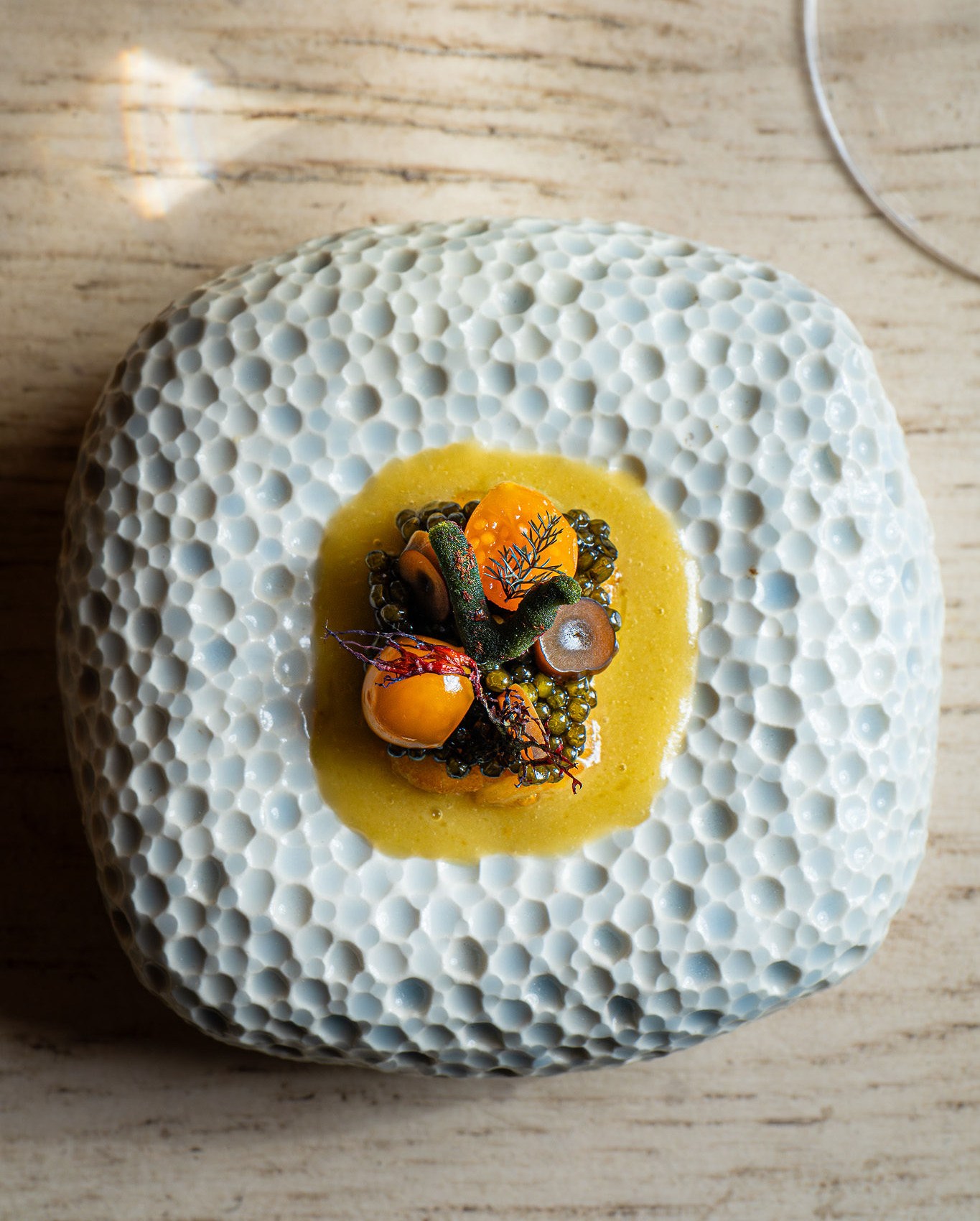 A plate of food with caviar, tomatoes, and herbs in a yellow sauce at Vicinity in Los Gatos.