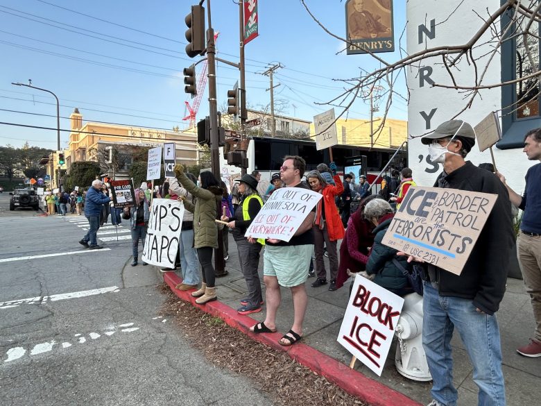 Several people stand on a street corner with protest signs, one of which says "ICE and border patrol are the terrorists"