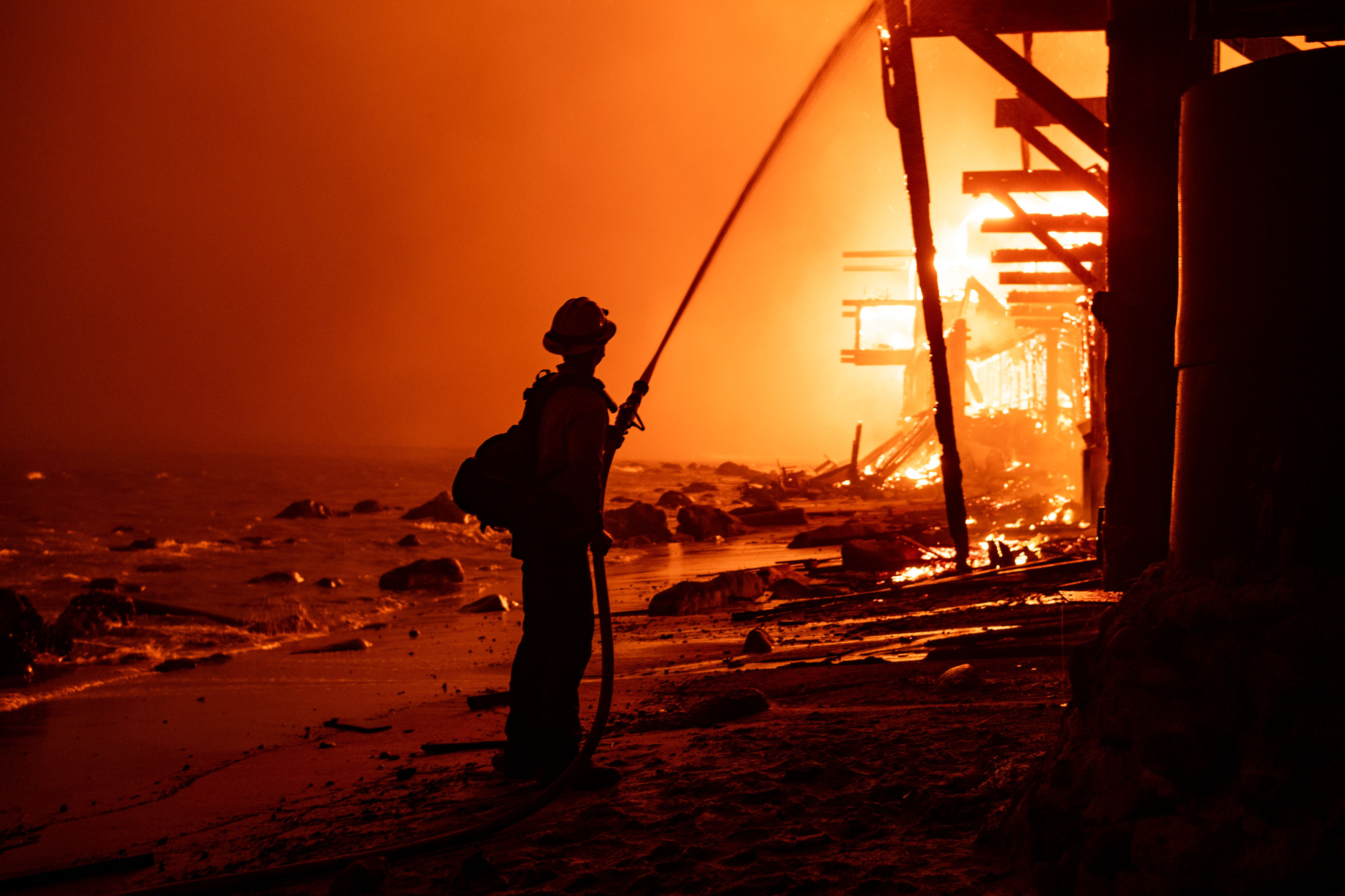 Firefighters battle fire from the surf as beachfront homes go...