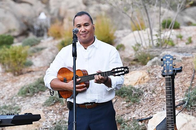 A man stands outdoors in front of a microphone, holding a ukulele