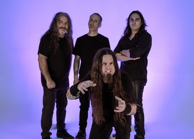 A man dressed in black kneels in the foreground, three other men dressed in black stand in the background.