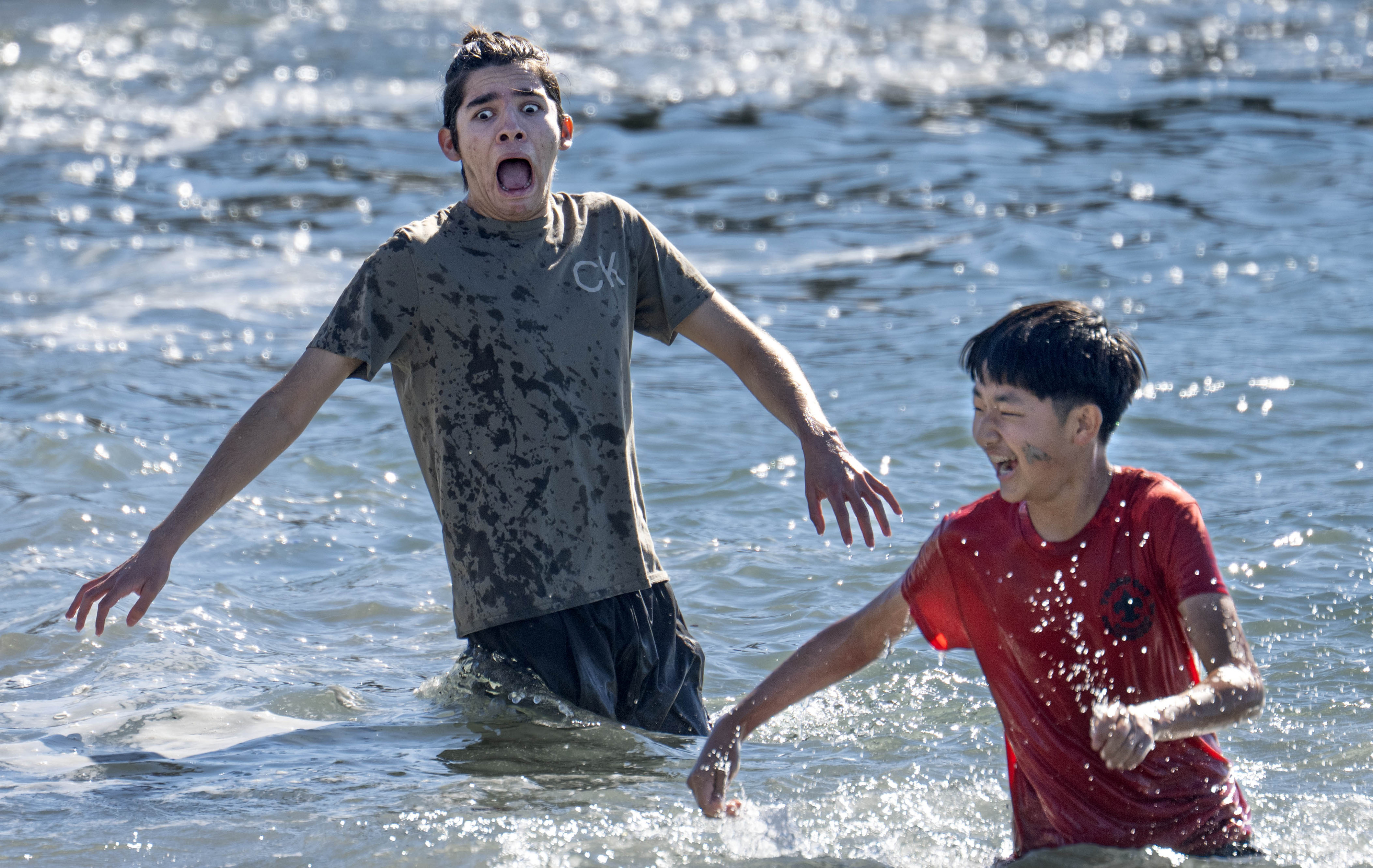 Cristian Martinez, 16, left, reacts to the cold water as...