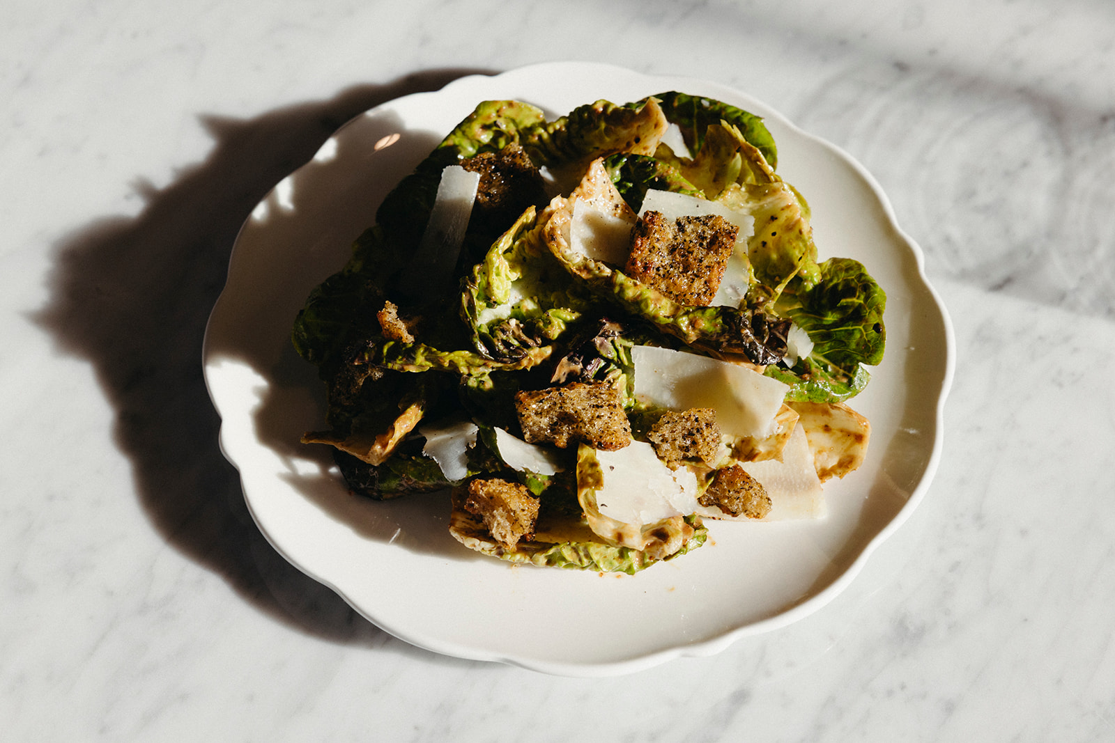 Caesar salad in the light with croutons on a marble countertop.
