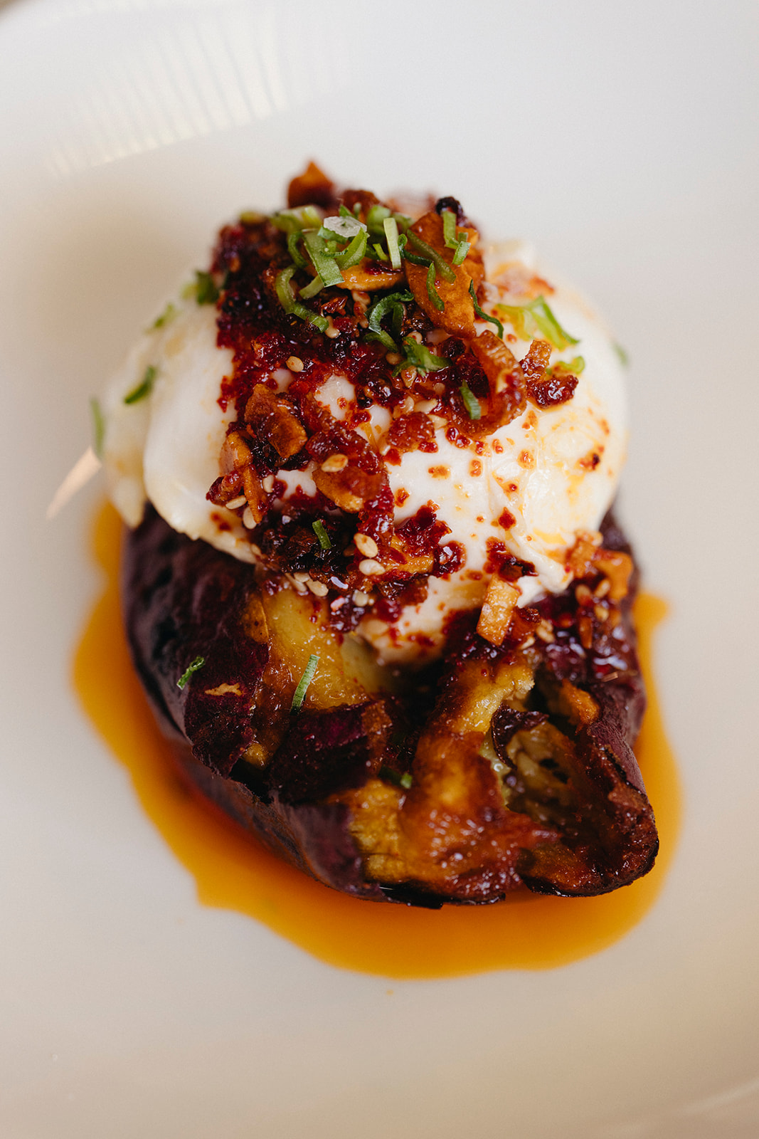 Burrata-topped roasted sweet potato with chile crisp on a white plate at Lapaba.