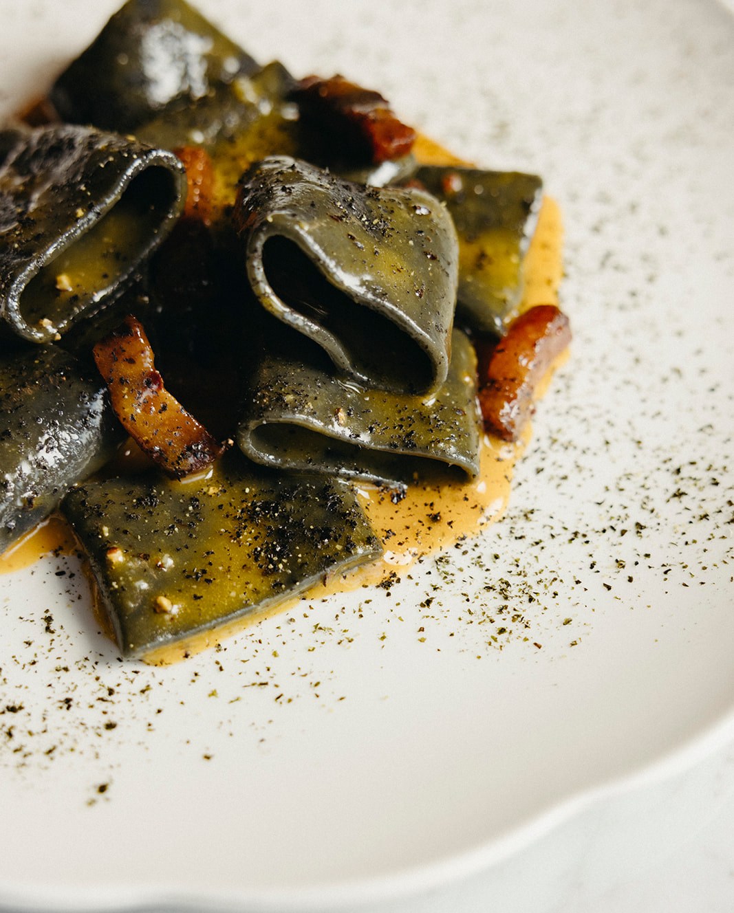 Close-up of rings of squid ink calamarata with kimchi on a white plate.