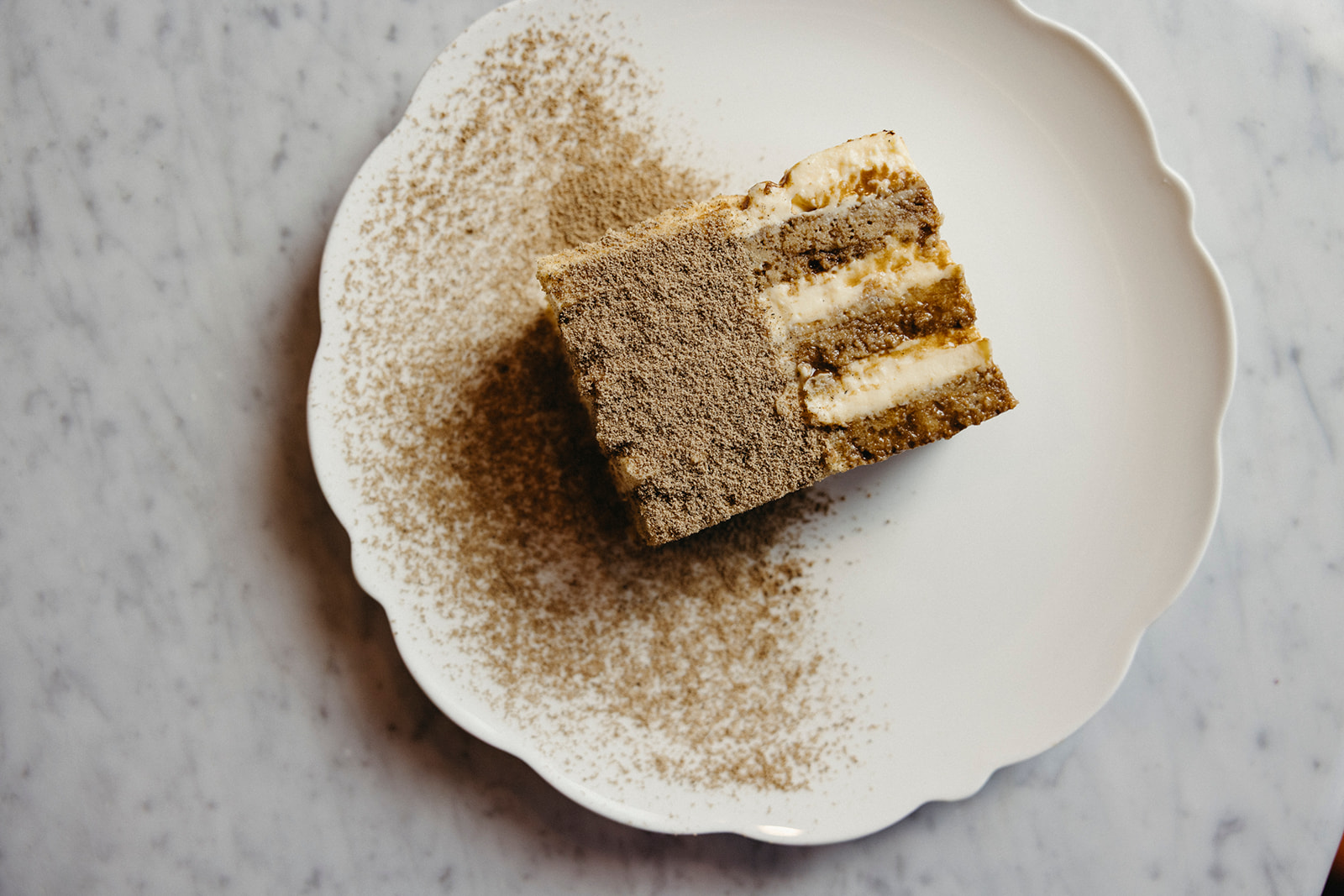 Slice of tiramisu with misugaru on a scalloped plate.