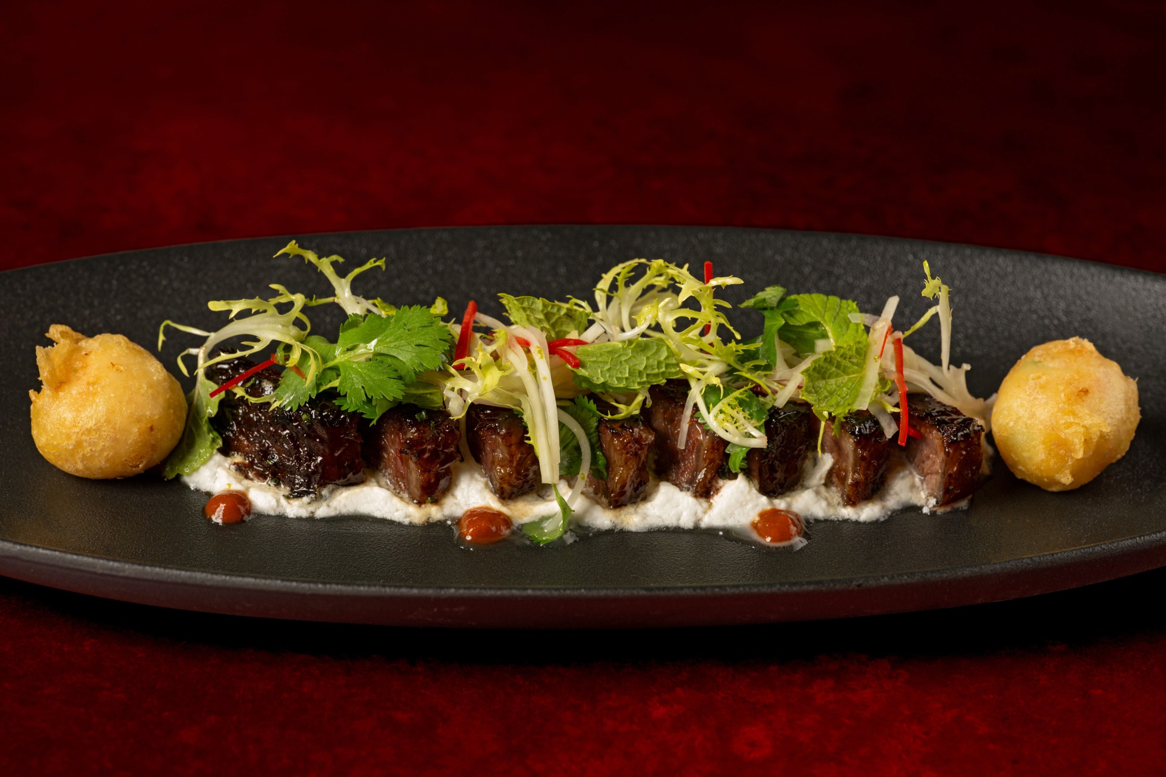 Sliced steak topped with greens on a bed of white sauce at Napa Rose