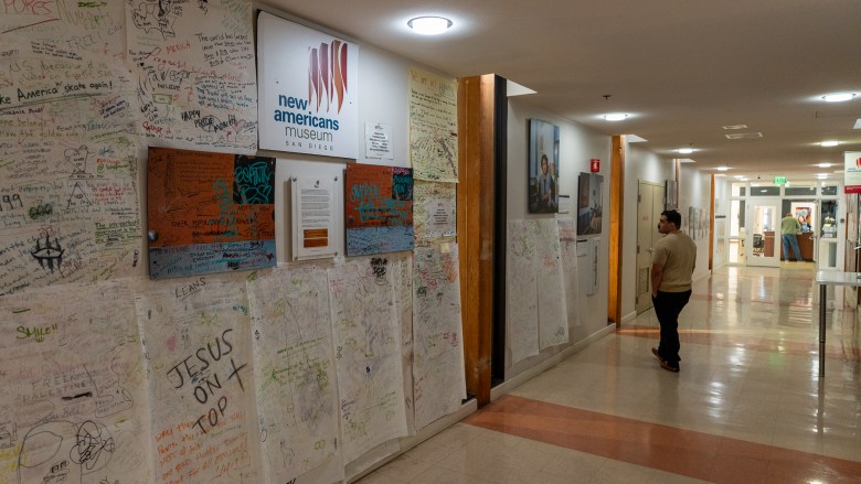 A hallway with walls covered in paper that people are invited to write upon. A person walks along looking at photographs.