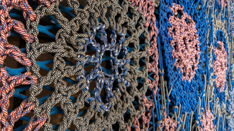 A web of multicolored cords creates circular patterns that extend across a frame dominated by blues and reds.