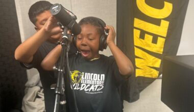 Image of a Black student with headphones over his ears singing into a microphone